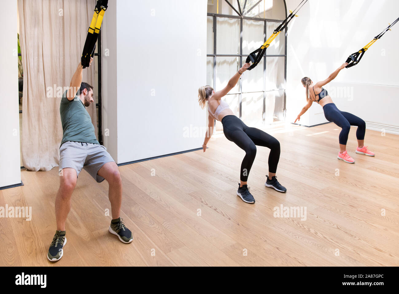 Three people working out doing Trx power pulls in a gym using suspended  straps and turning their upper bodies Stock Photo - Alamy