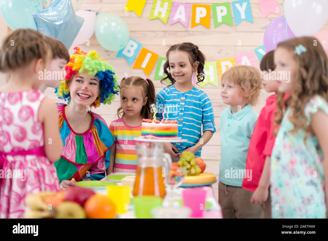 Birthday children party. Kids with clown gathered around birthday cake Stock Photo
