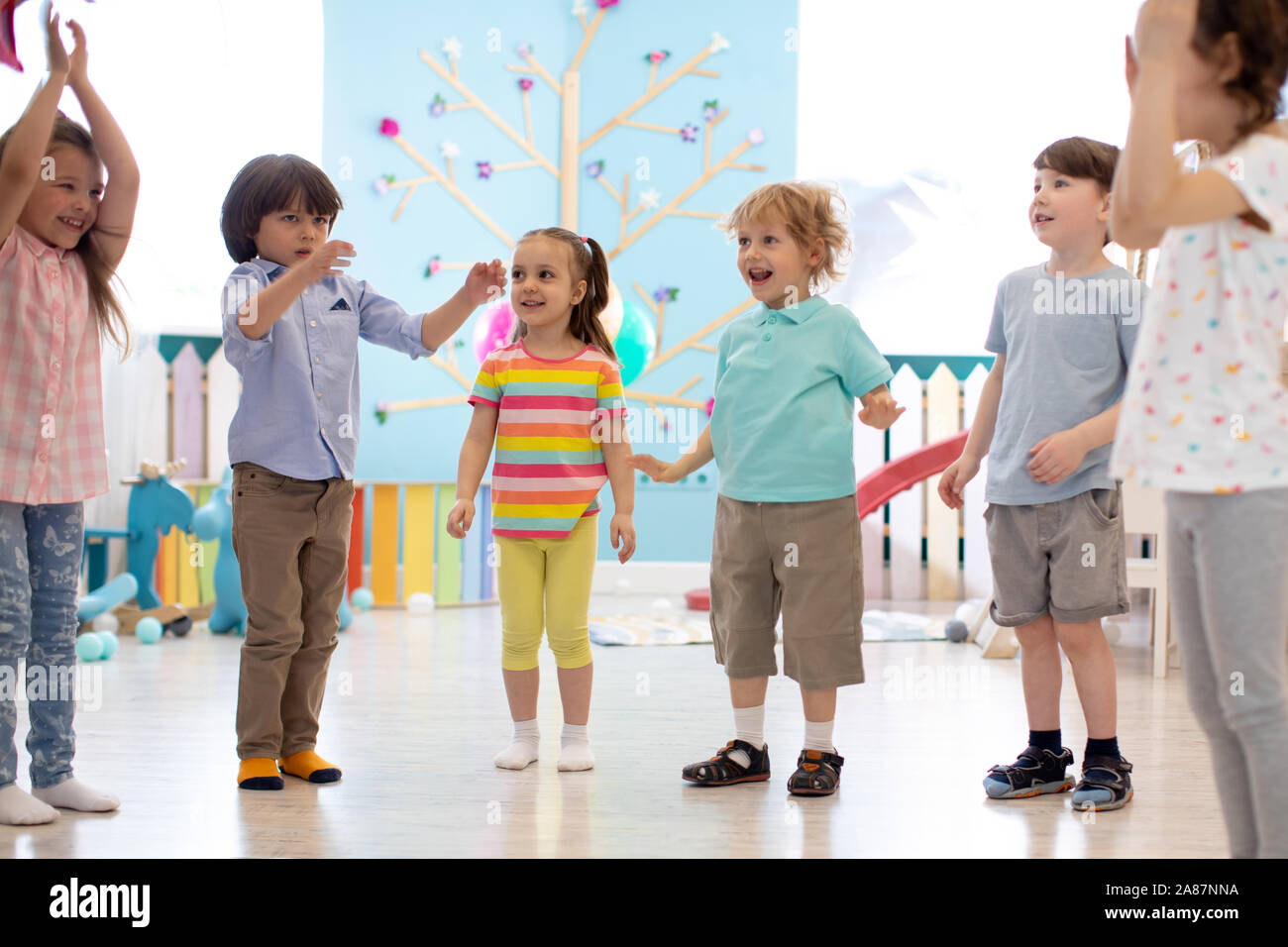 Happy children stand semicircle on floor in kindergarten or day care centre. Preschool kids have fun indoors, playing games Stock Photo