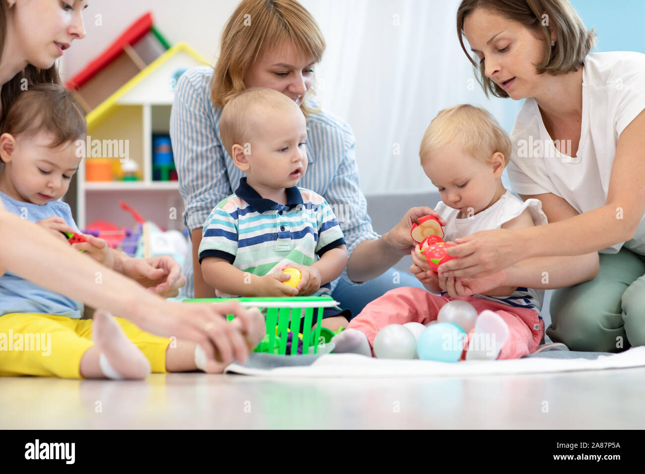 Toddler babies with moms in playroom in nursery Stock Photo