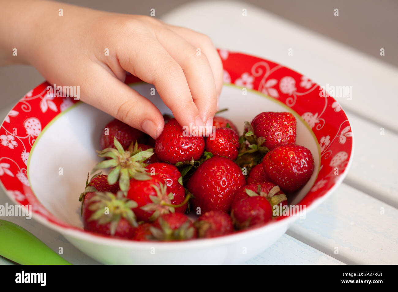 Close up of little girl taking from strawberry bowl. Stock Photo