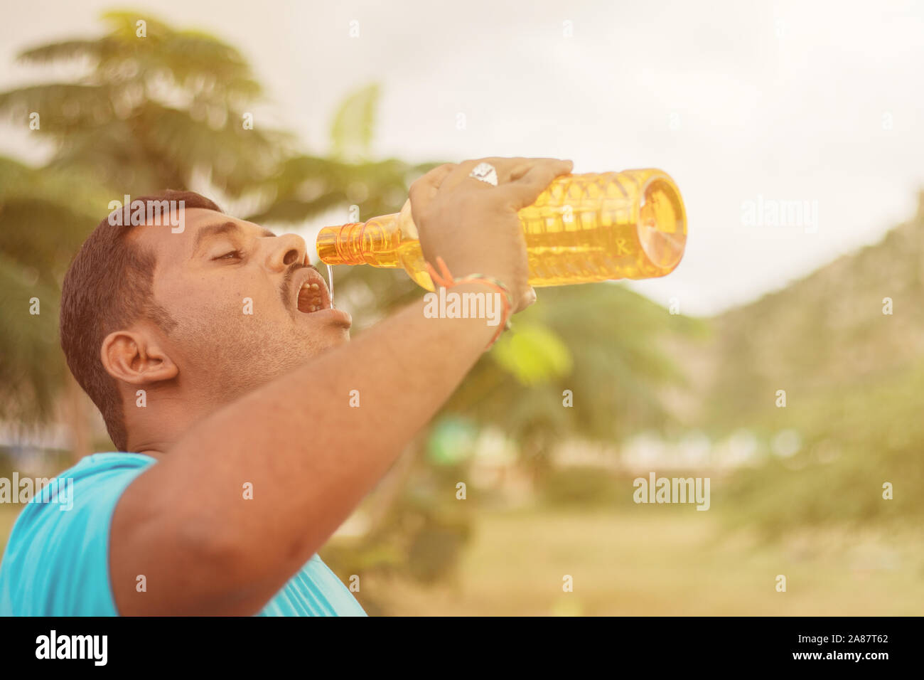 Fat young man drinking water from bottle outdoor - Thirsty obese man drinking water after exercise. Stock Photo