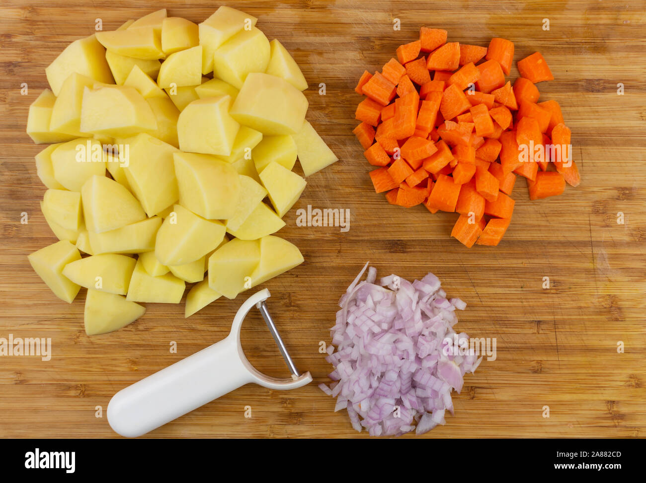 https://c8.alamy.com/comp/2A882CD/view-of-a-wooden-cutting-board-with-pieces-of-potatoes-onions-carrots-and-a-white-food-peeler-2A882CD.jpg