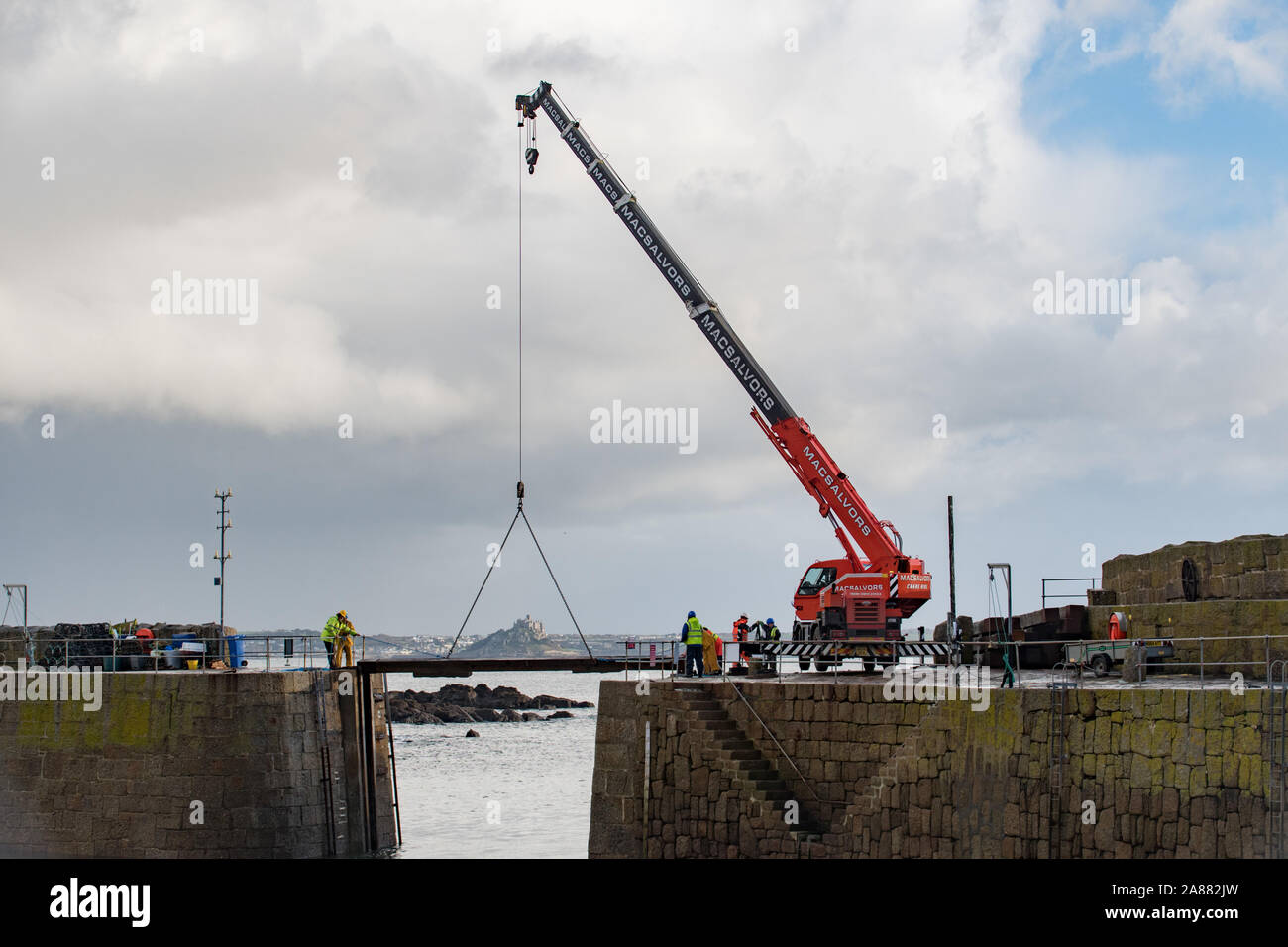 Mousehole, Cornwall, UK, 7th November 2019. UK Weather. Every year giant timber baulks are lowered carefully into the opening of Mousehole harbour,  to protect it from the winter storms. Seen in the background St Michaels Mount at Marazion. Credit Simon Maycock / Alamy Live News. Stock Photo