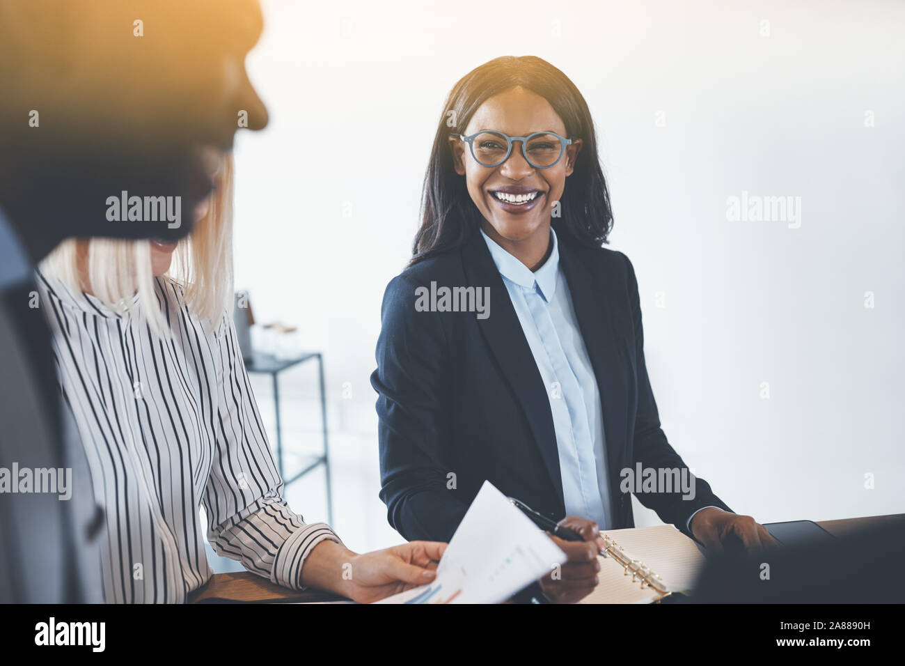 Laughing African American businesswoman talking with coworkers while having a meeting together in an office Stock Photo