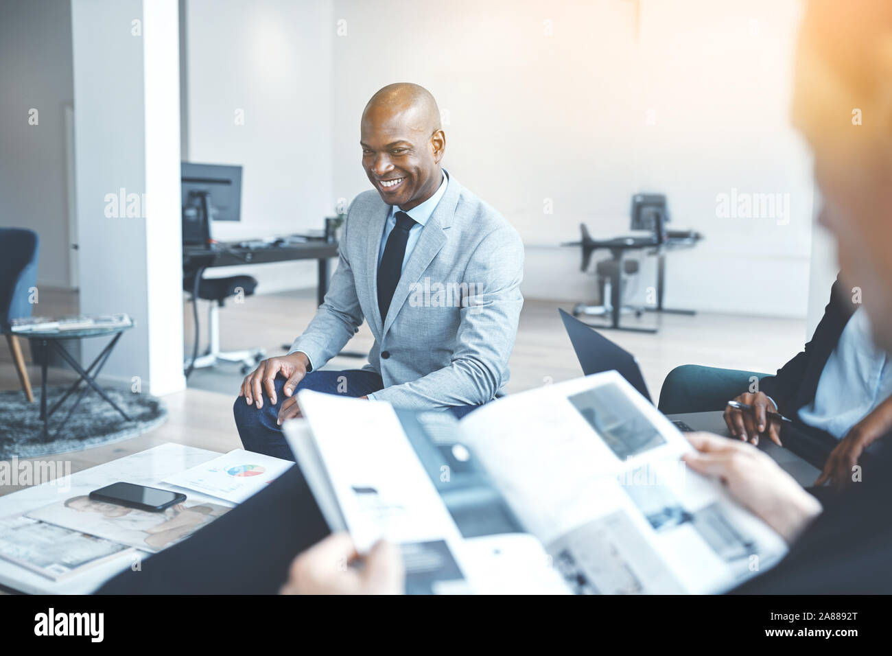Young African American businessman laughing during a casual meeting with a group of colleagues in an office Stock Photo