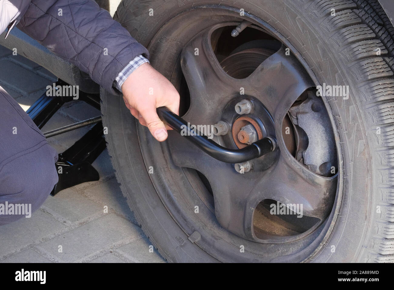 Driver is screwing and unscrewing changing car wheel by wrench. Damaged