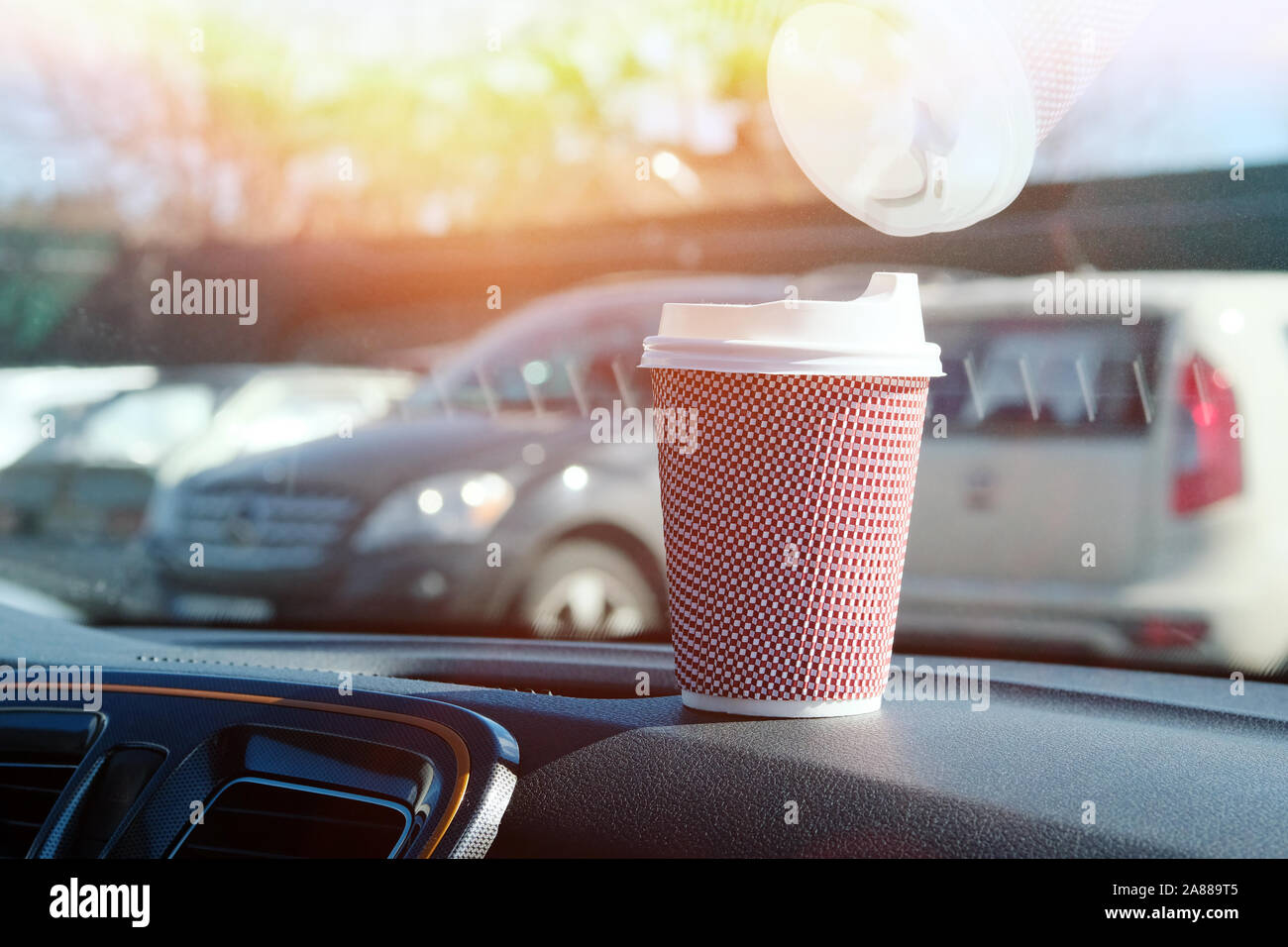 Paper cup with tea or coffee in car on sunny blurred background. Takeaway. Morning breakfast in auto. Stock Photo