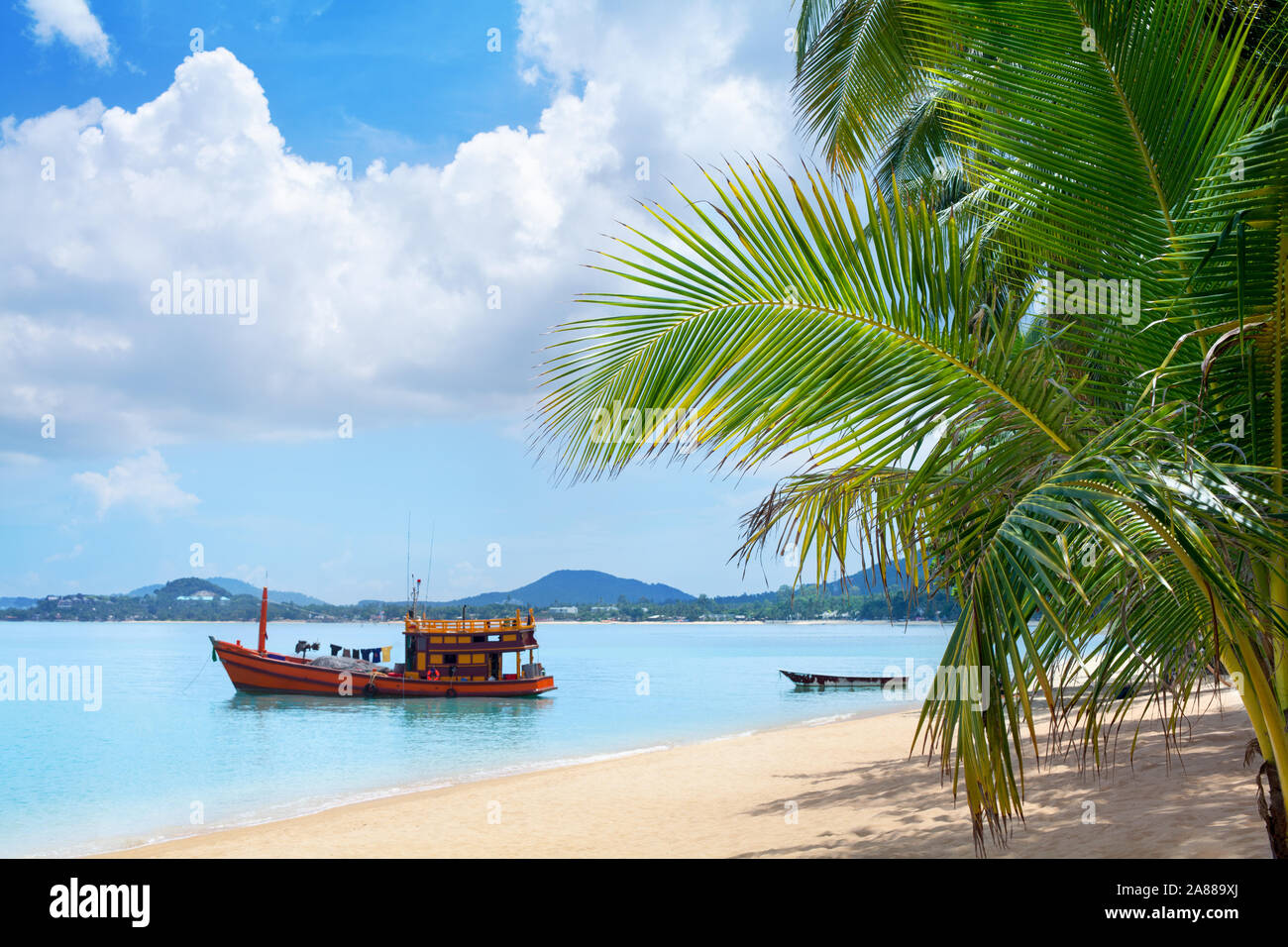 Tropical white sand beach landscape, turquoise sea water, blue sky, clouds, green palm tree leaves, boat, sunny day, nobody, relax on exotic island Stock Photo
