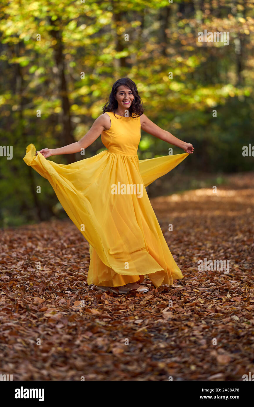 Happy young woman in long yellow dress dancing in an autumn landscape ...