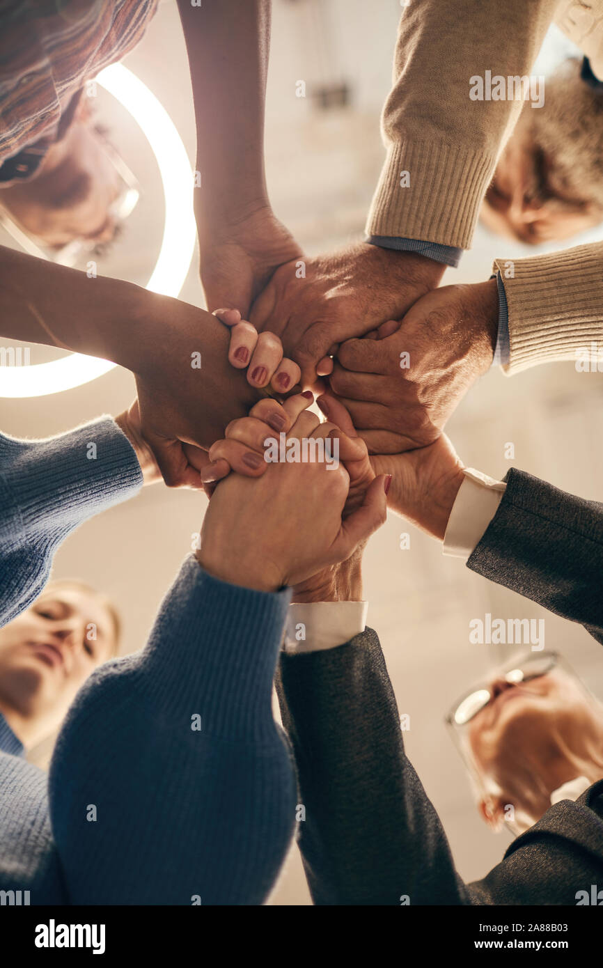 Low angle view of group of people holding hands and uniting during team work at meeting Stock Photo