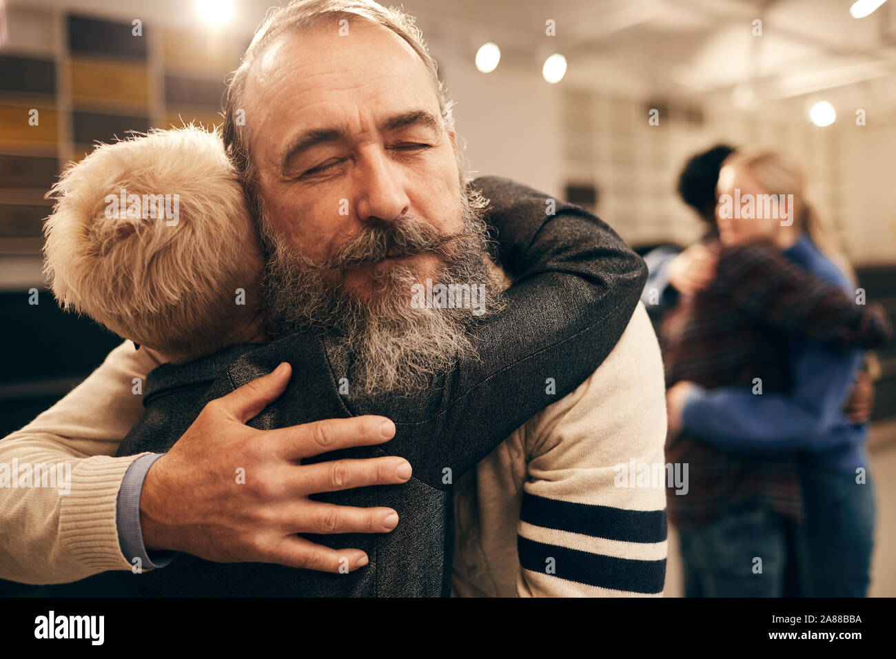 Senior bearded man embracing woman and enjoying the hug during therapy with other couple in the background Stock Photo