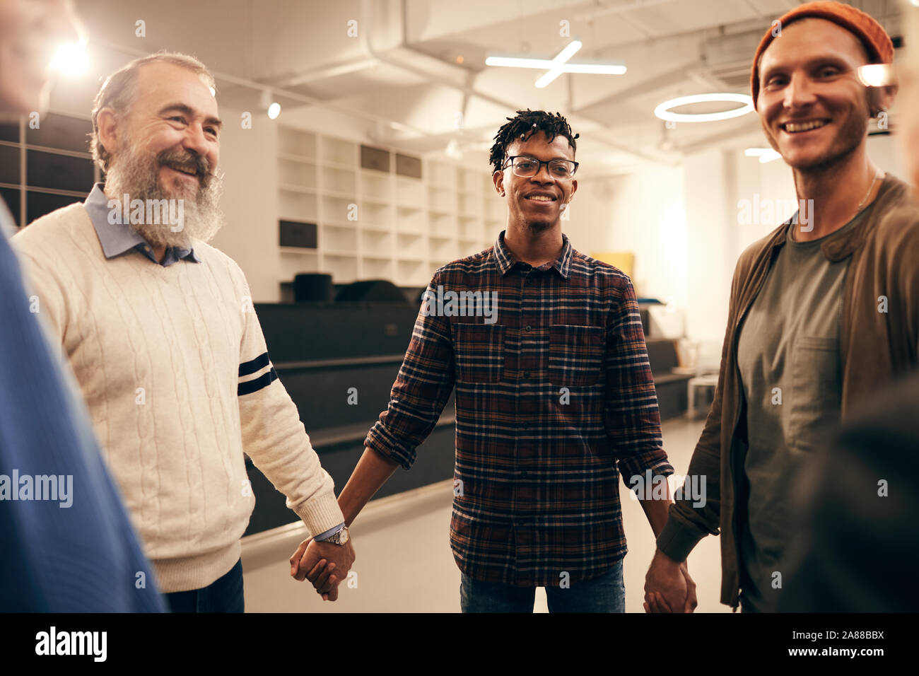Group of happy people standing holding hands and smiling to each other during business training at office Stock Photo