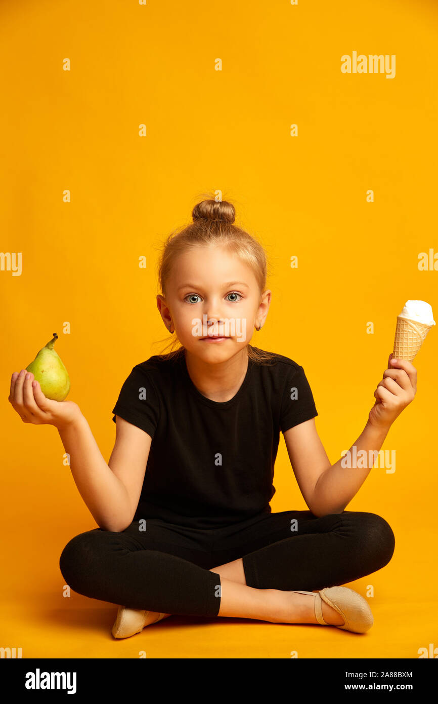 Puzzled little dancer choosing between pear and ice cream Stock Photo