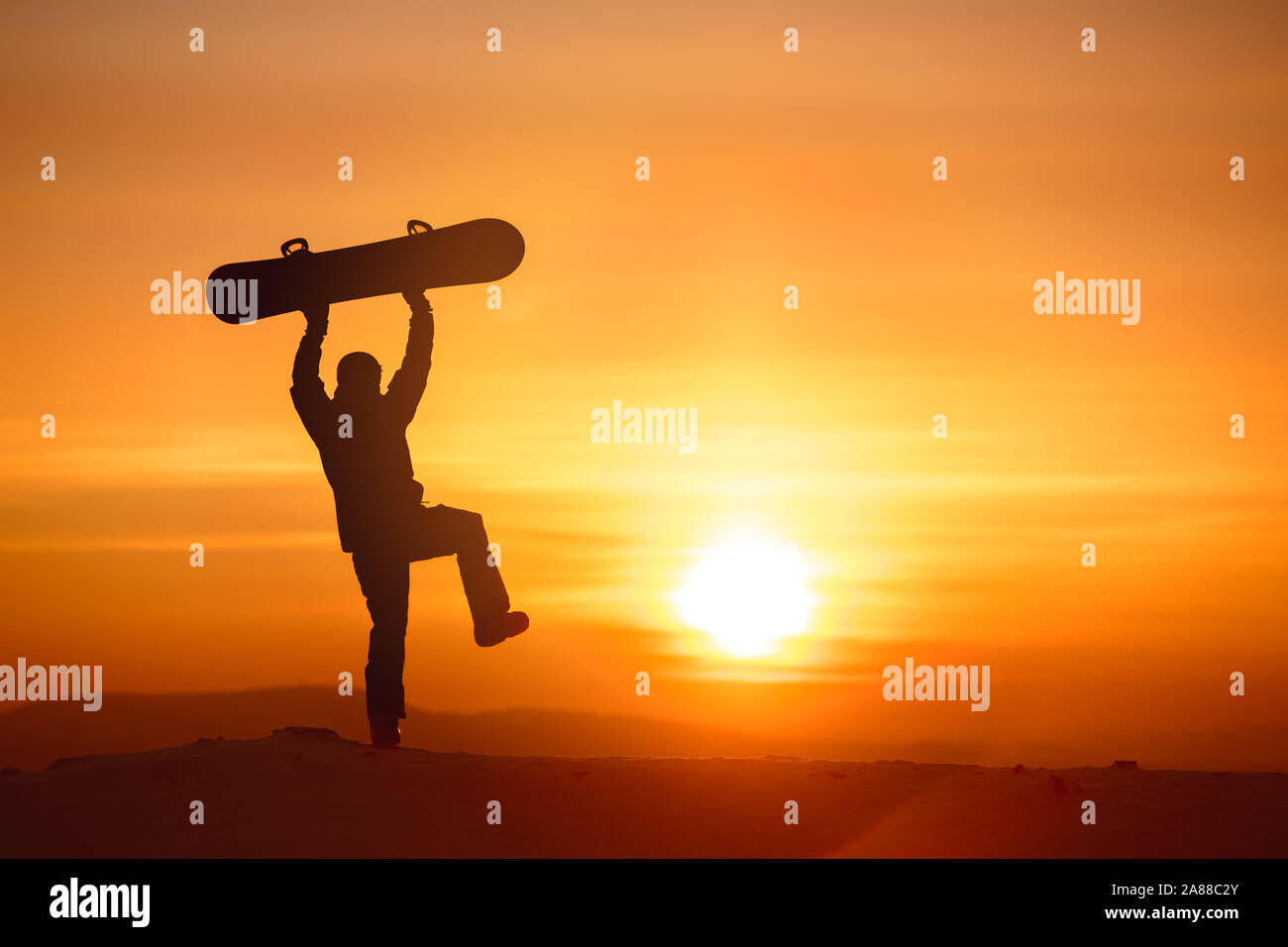 Happy snowboarder is dancing with snowboard above head against sunset sky and light Stock Photo