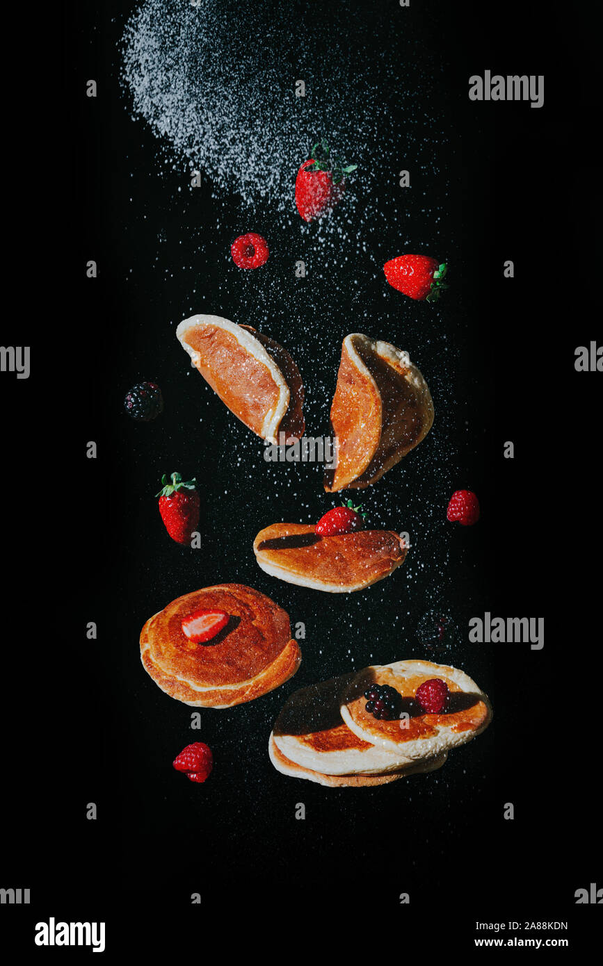 Flying pancakes with sugar and berries captured on black background Stock Photo