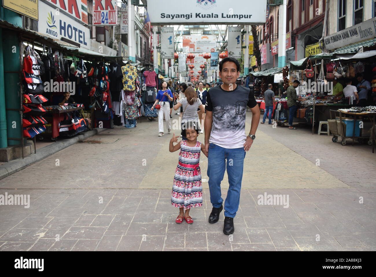 A man wearing jeans and t-shirt, with his daughter walking on empty road of a china town of Kuala Lumpur, Malaysia Stock Photo