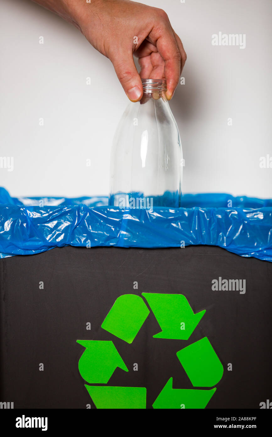 Hand putting glass bottle into recycling bin. Person in a house kitchen separating waste. Black