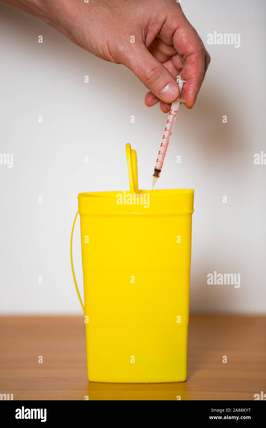 Hand putting used syringe with needle into yellow bin for safe disposal. Person separating dangerous waste. Medical waste management Stock Photo