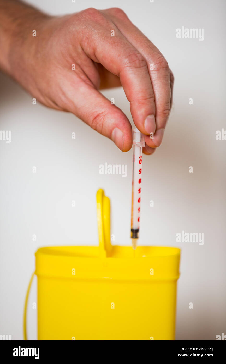Hand putting used syringe with needle into yellow bin for safe disposal. Person separating dangerous waste. Medical waste management Stock Photo
