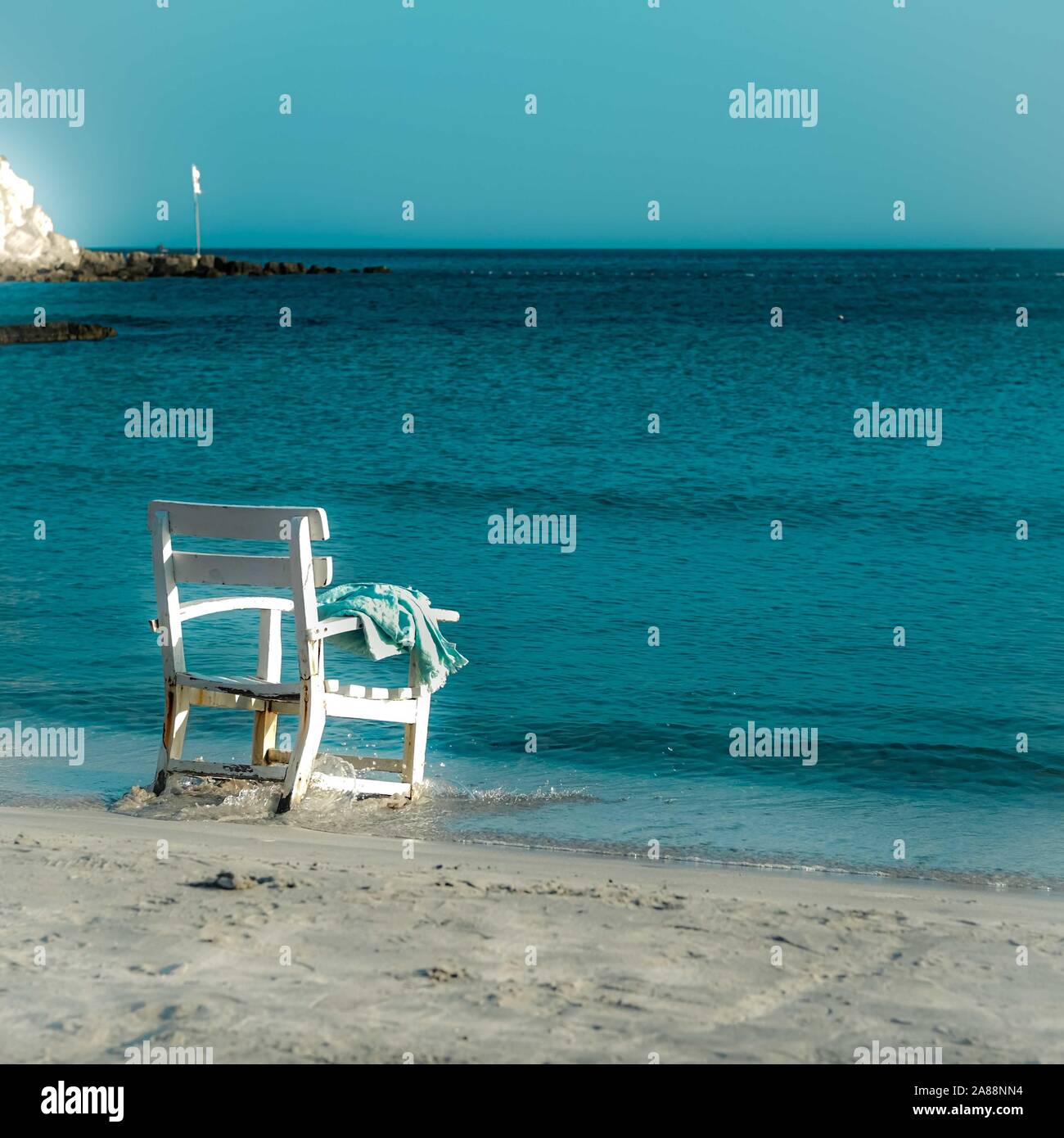 Lonly shabby white chair and blue towel left at the armrest facing the blue Mediterranian sea. Solitude concept. Cesme, Izmir, Turkey. Square format. Stock Photo