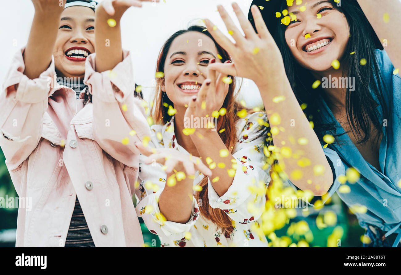 Happy Asian friends having fun throwing confetti outdoor - Young trendy people celebrating at festival event outside Stock Photo