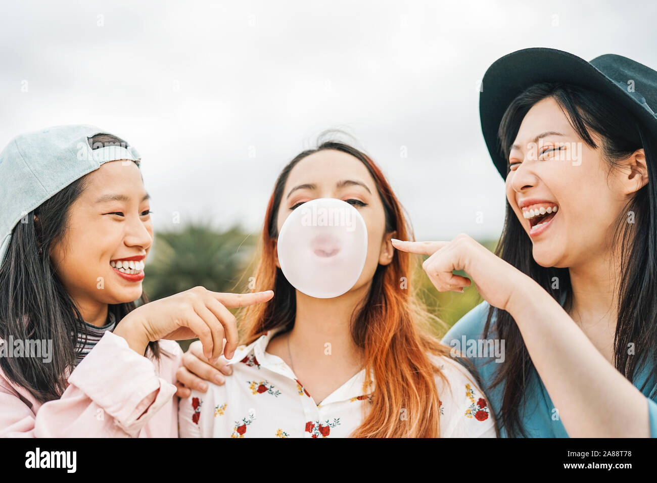 Happy Asian friends having fun with chewing bubble gum outdoor - Young people playing and laughing together Stock Photo