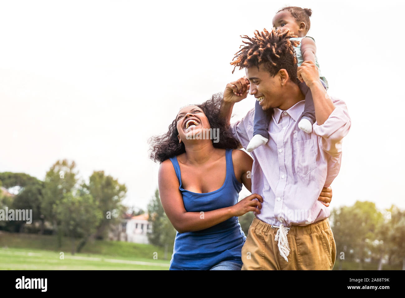 Happy African family enjoying together in public park - Mother, father and daughter having fun during a weekend sunny day outdoor Stock Photo