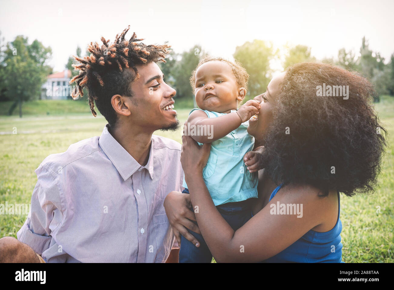 Happy black family enjoying a tender moment during the weekend outdoor - Mother and father having fun with their daughter in a public park Stock Photo