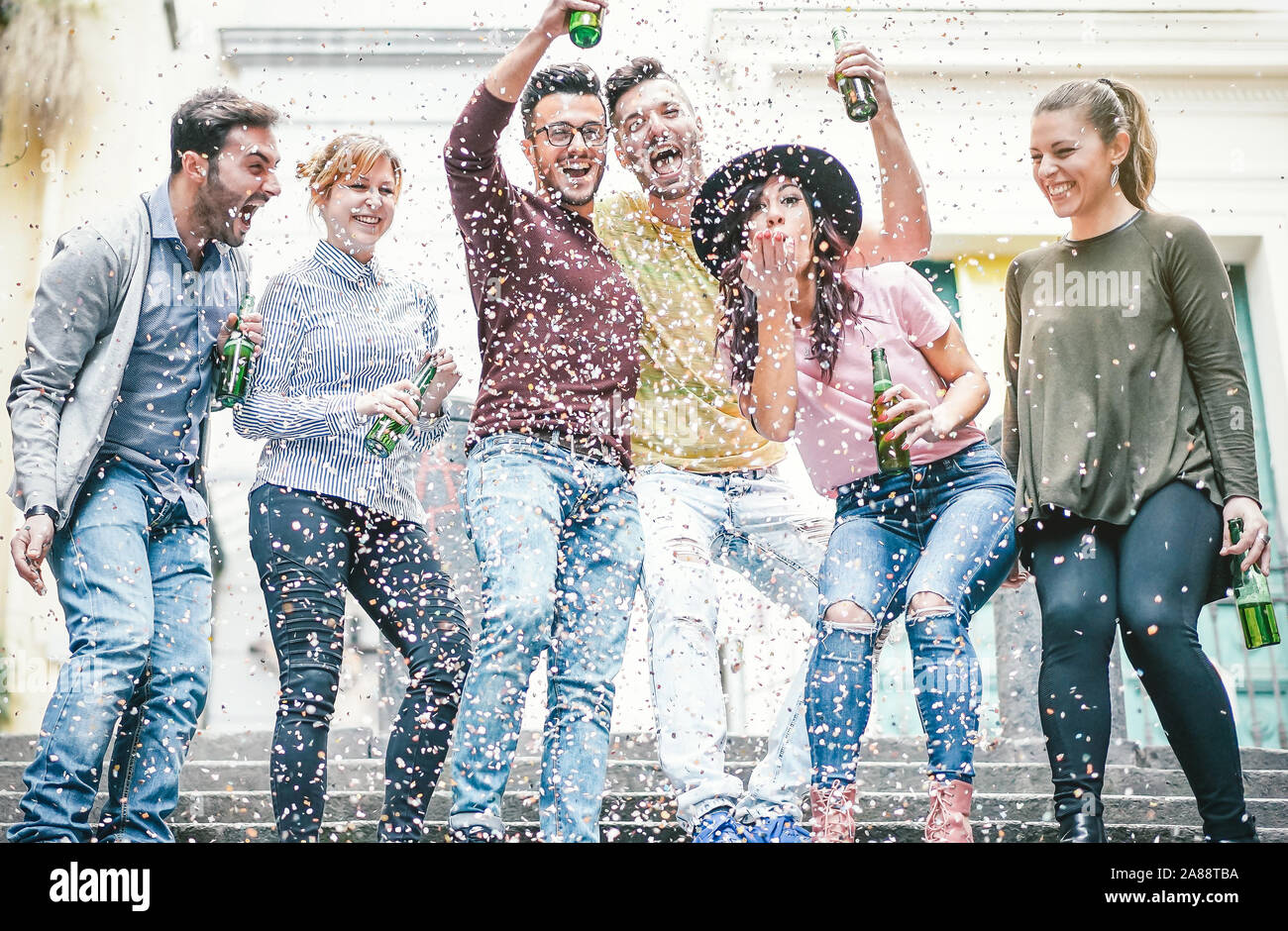 Group of happy friends doing party drinking beer and throwing confetti - Young millennial people having fun celebrating birthday and laughing together Stock Photo