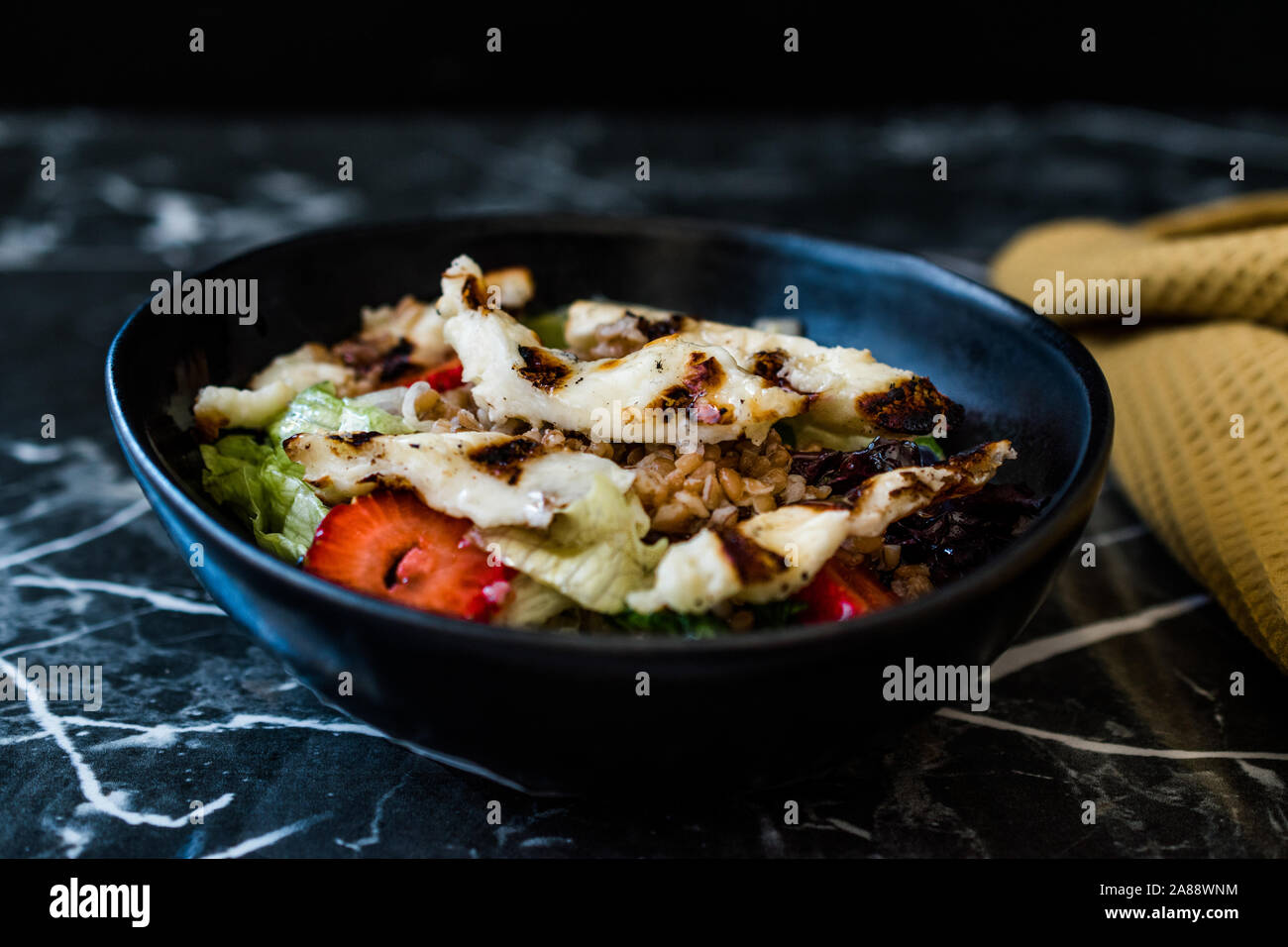 Grilled Halloumi Cheese Salad with Strawberry Slices and Buckwheat / Hellim in Black Bowl on Dark Granite Surface. Organic Fresh Food. Stock Photo