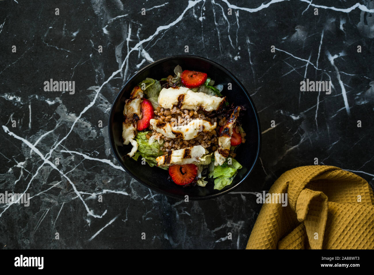 Grilled Halloumi Cheese Salad with Strawberry Slices and Buckwheat / Hellim in Black Bowl on Dark Granite Surface. Organic Fresh Food. Stock Photo