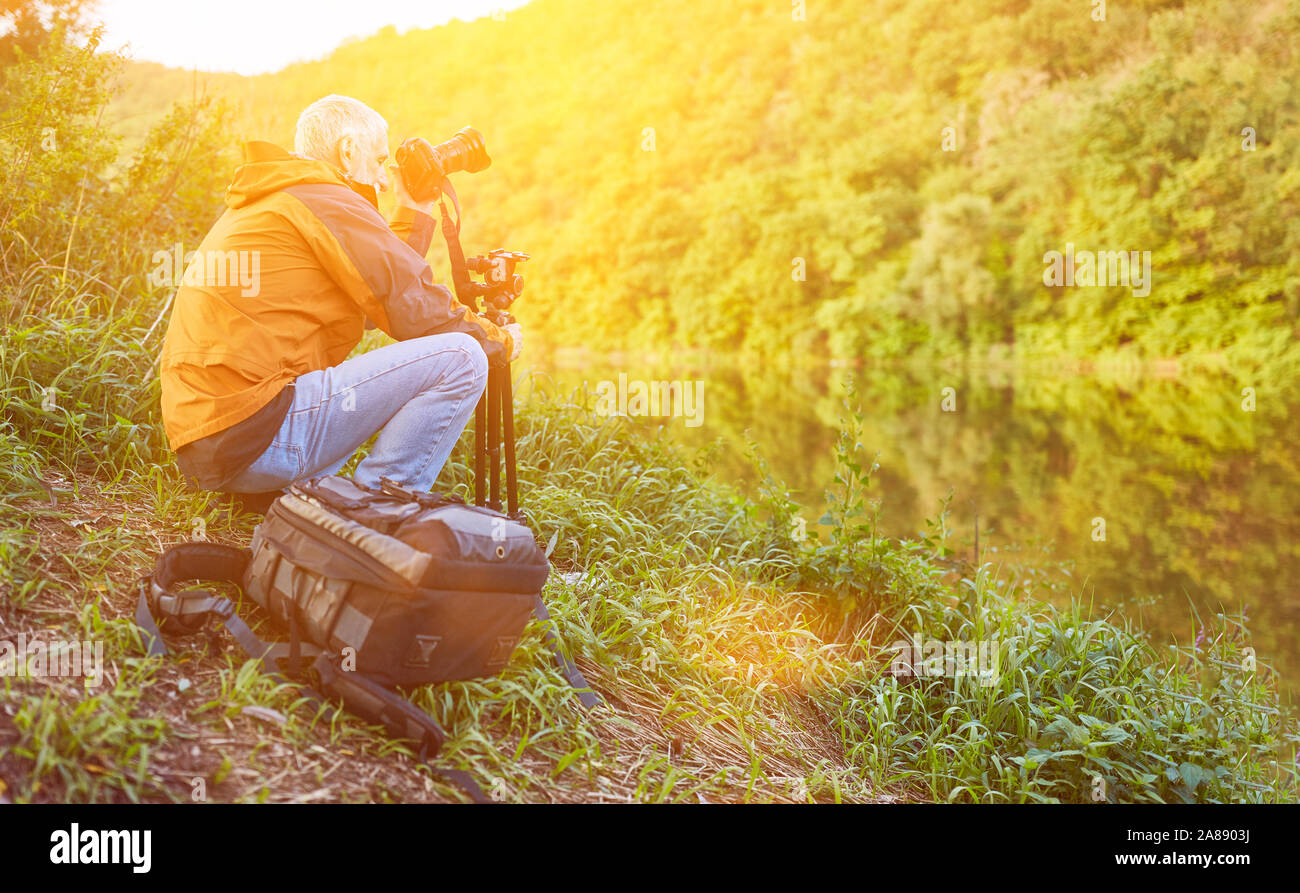 Old landscape photographer in nature at the river while photographing Stock Photo