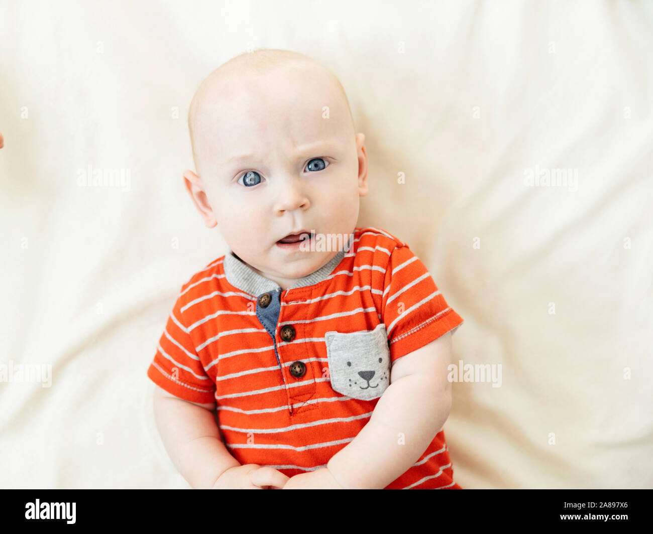 Confused baby boy lying on bed Stock Photo