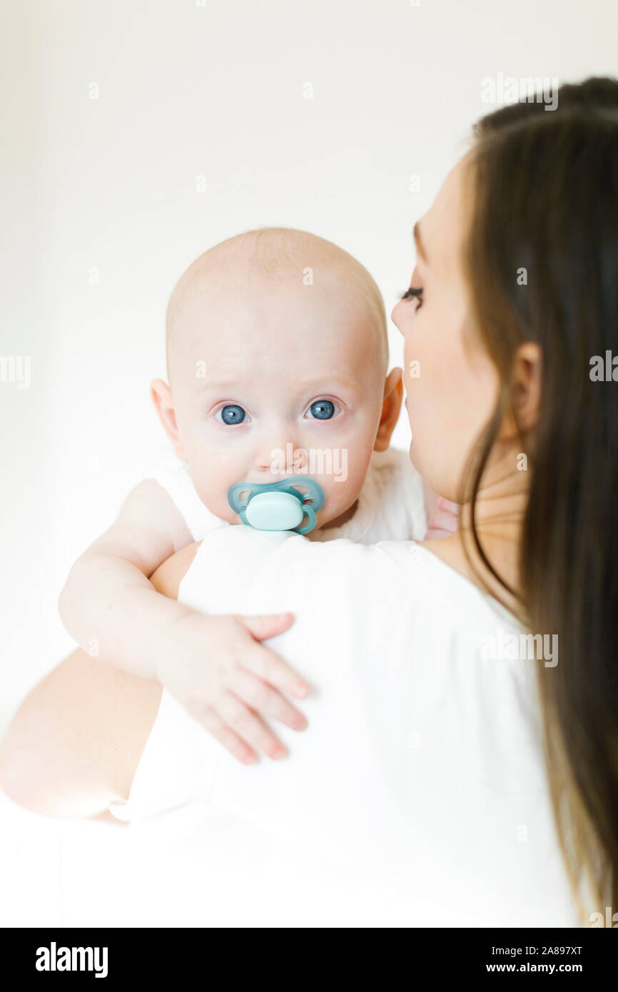 Baby boy using pacifier looking over his mother's shoulder Stock Photo