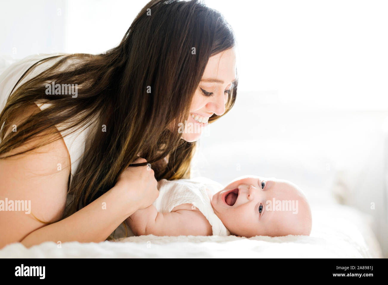 Smiling mother lying with her son on bed Stock Photo
