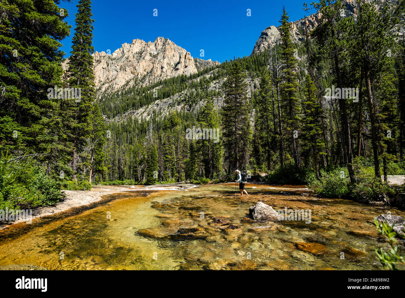 Woman wading through river by Sawtooth Mountains in Stanley, Idaho, USA Stock Photo