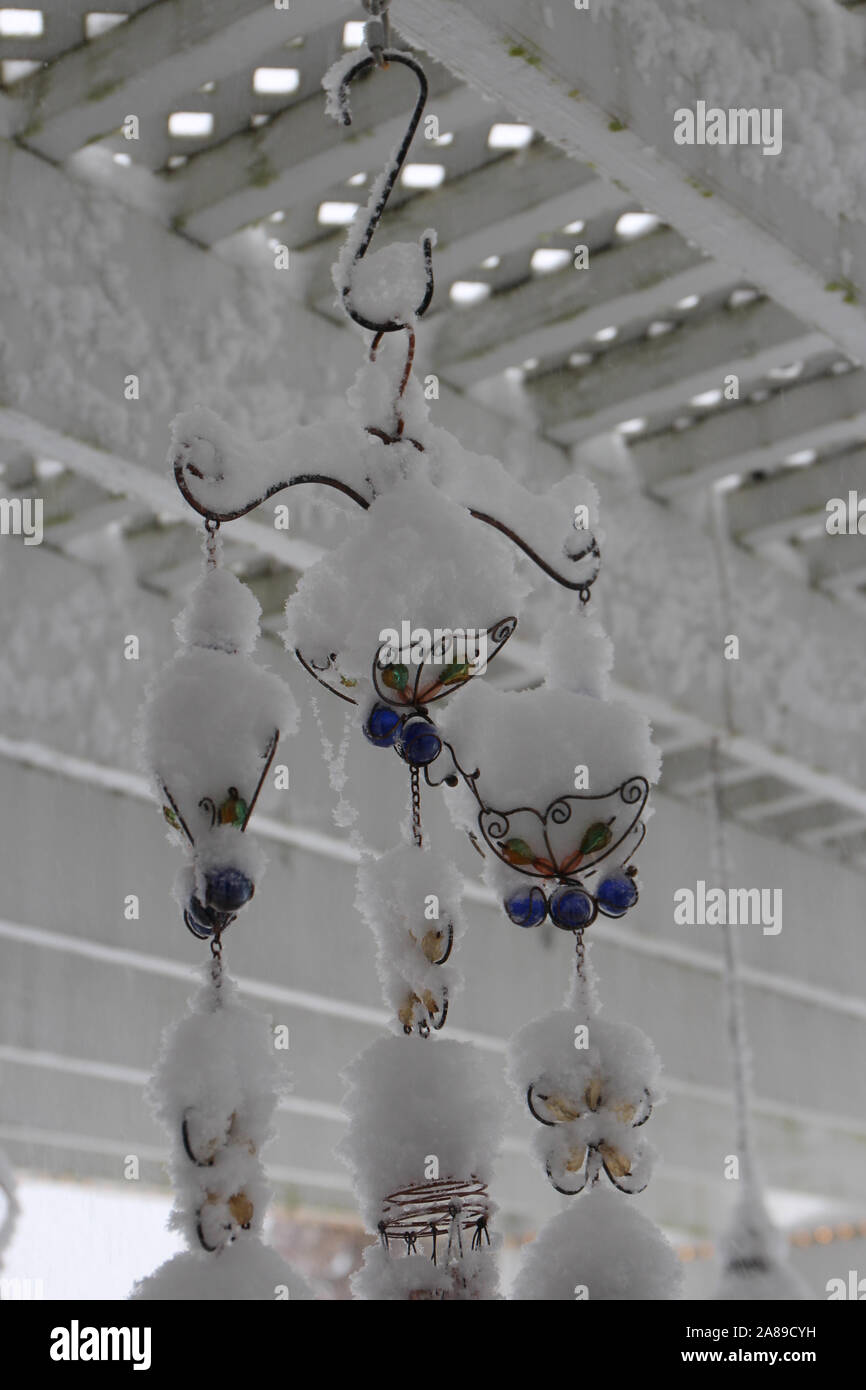 A butterfly windchime hanging from a white, wood pergola covered in snow in the fall in Wisconsin, USA Stock Photo