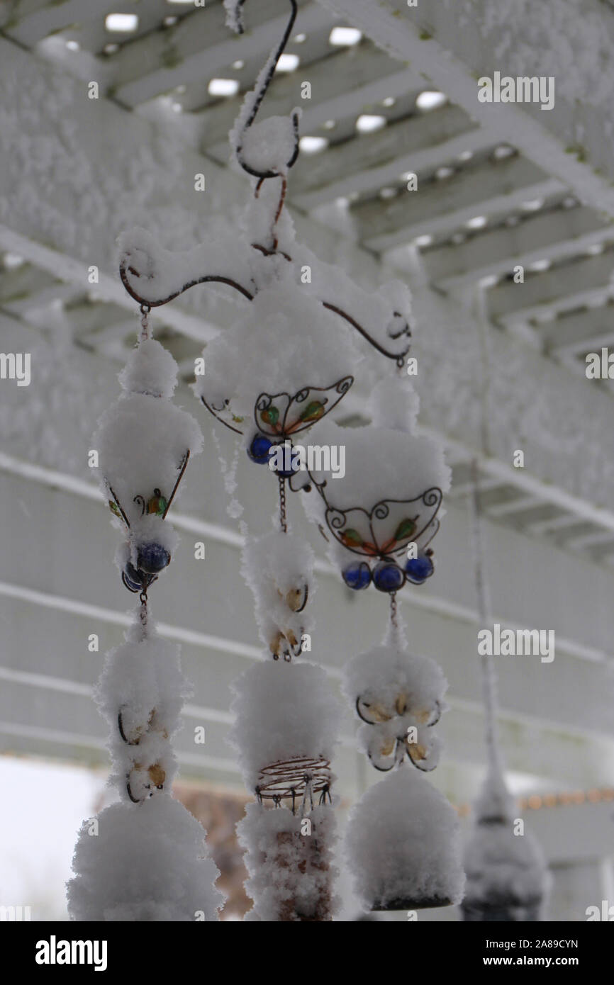 A butterfly windchime hanging from a white, wood pergola covered in snow in the fall in Wisconsin, USA Stock Photo