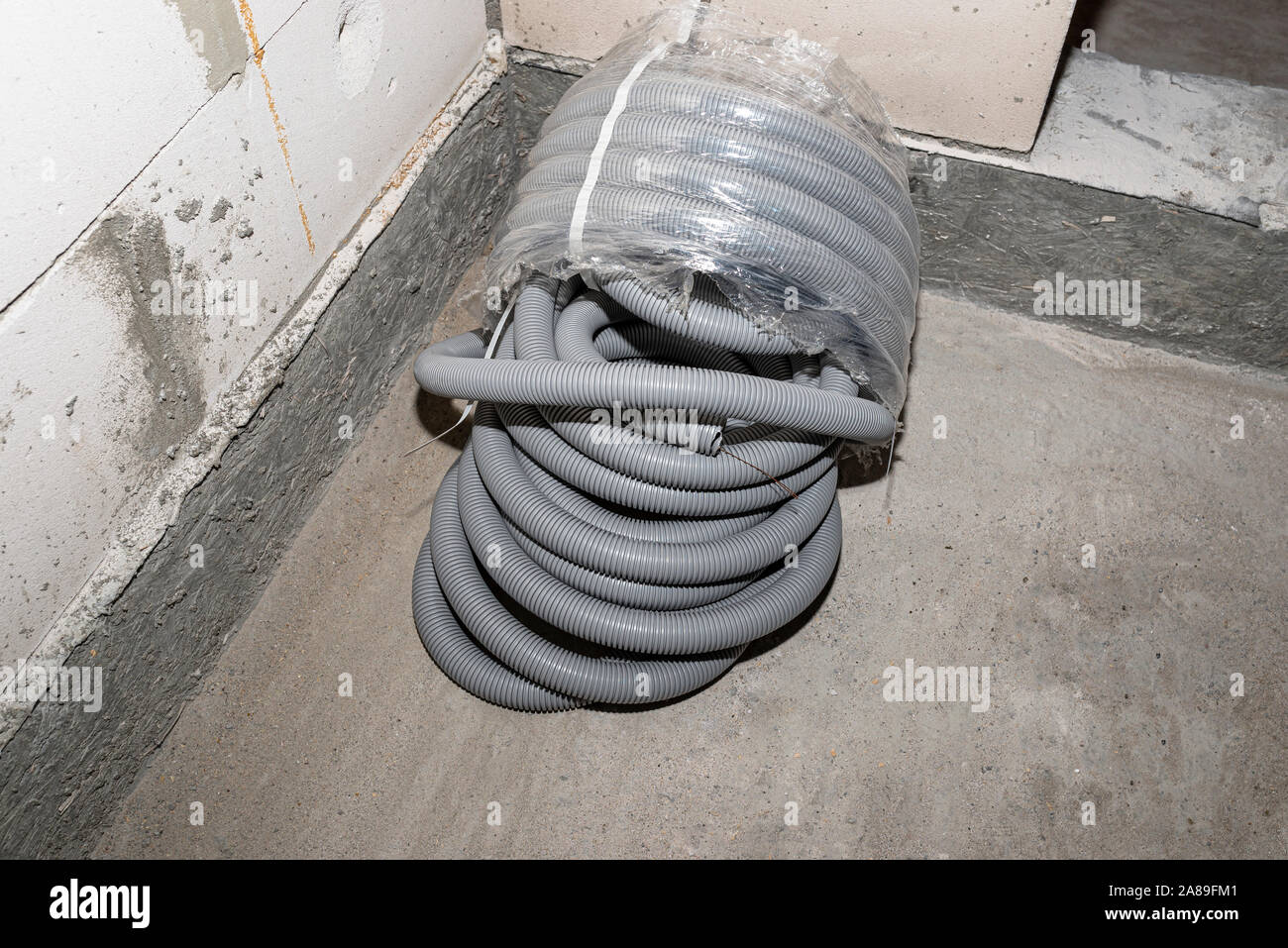 PVC corrugated pipe for electric wires, partly unpacked, lying on the floor in the house. Stock Photo