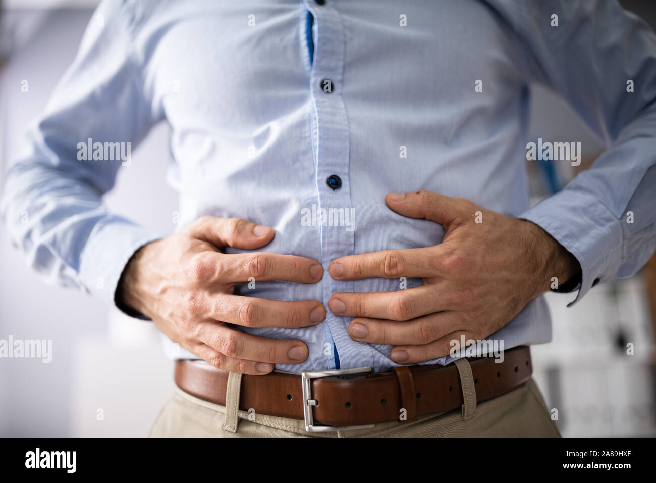 Midsection Of Businessman Suffering From Stomach Ache Against White Background Stock Photo