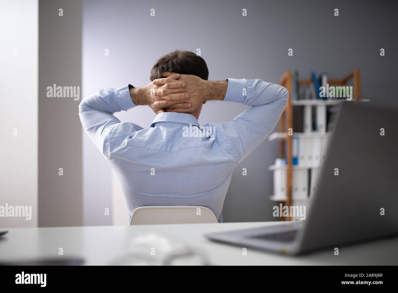 Relaxed Businessman With Hands Behind Head Sitting In Office Stock Photo