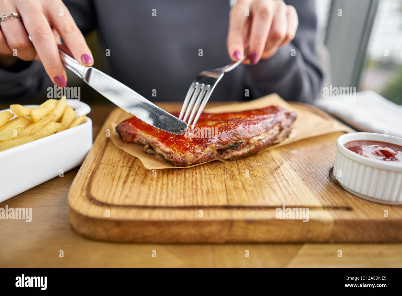 Lunch in a restaurant, a woman cuts Delicious Pork ribs. Full rack of ribs BBQ on wooden plate with french fries and salad Stock Photo