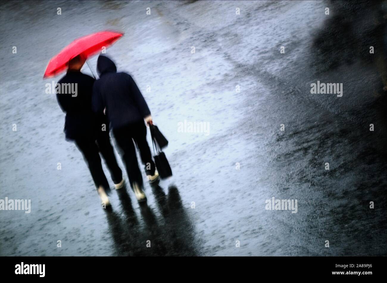 Couple walking through the rain with a bright red umbrella Stock Photo