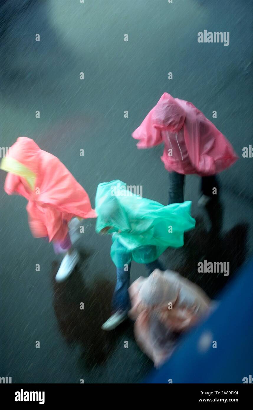A group of people in colorful raincoats running through the streets in the rain Stock Photo