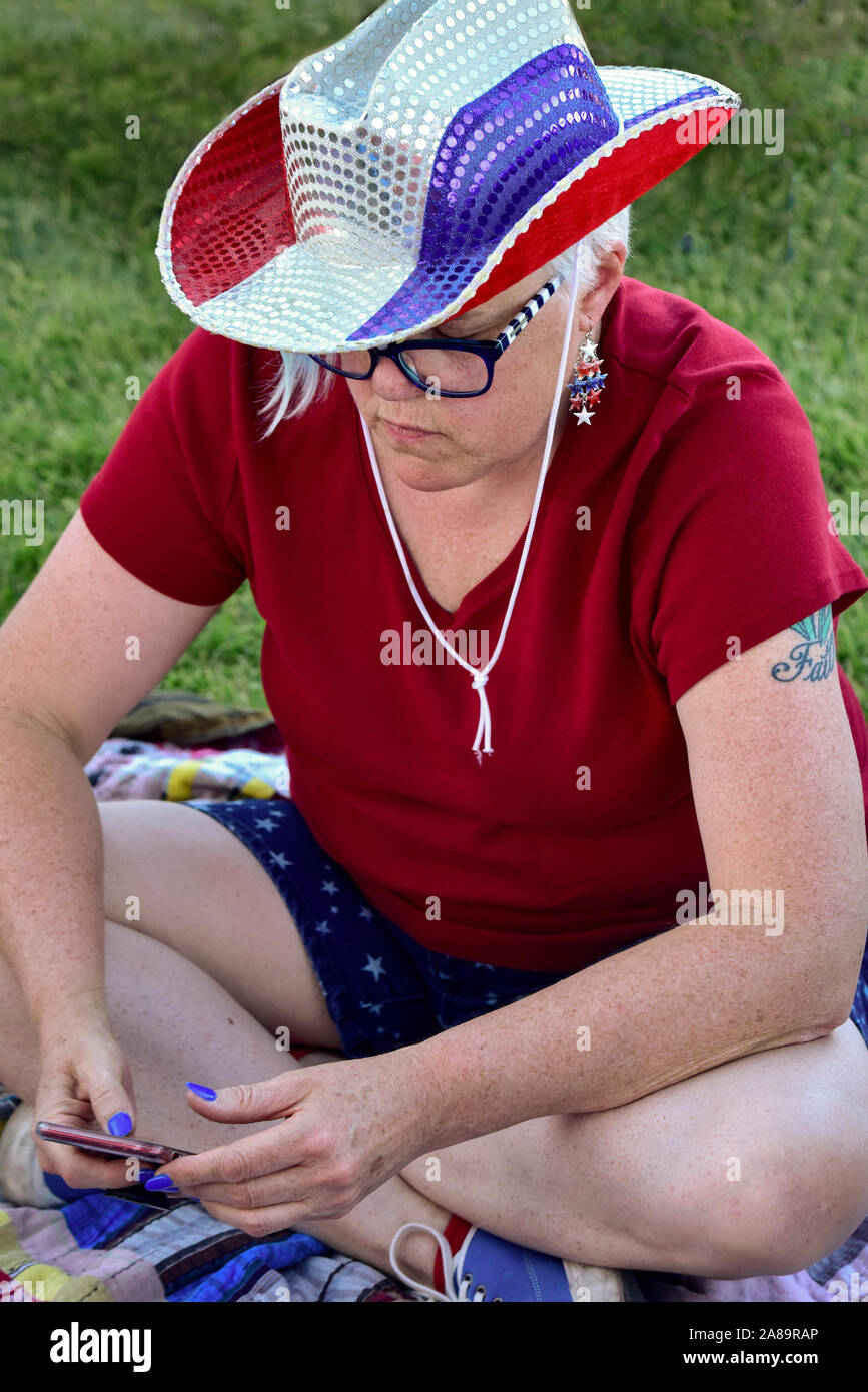 Festival goer having fun on a sunny Independence Day wearing a Red White and Blue hat and looking at her phone. Stock Photo