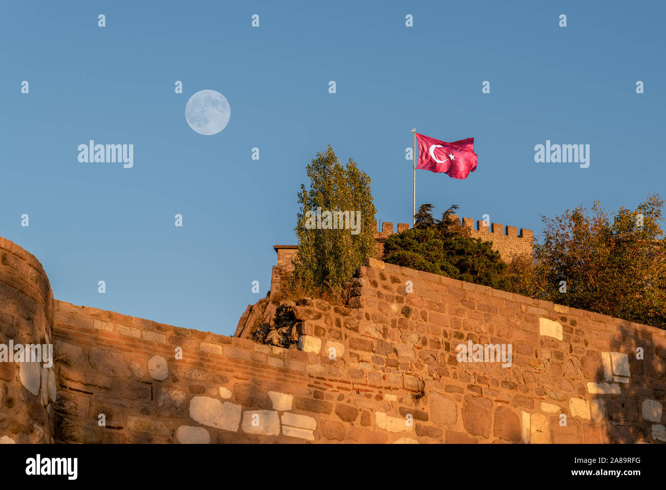 Closeup of Ankara Castle on blue sky background with flying flag under moon Stock Photo