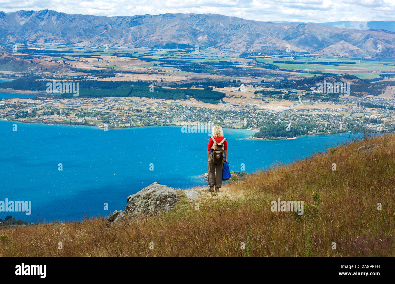 Panoramic view of lake Wanaka, New Zealand. Wanaka lake and woman in red shirt standing on the top of mountain Stock Photo