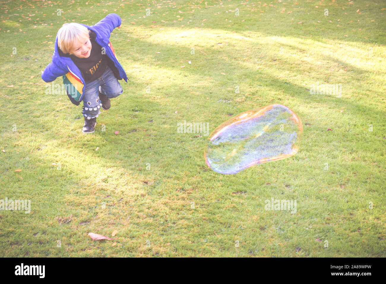 Child playing outside in a garden during day time with bubbles he is happy and running Stock Photo