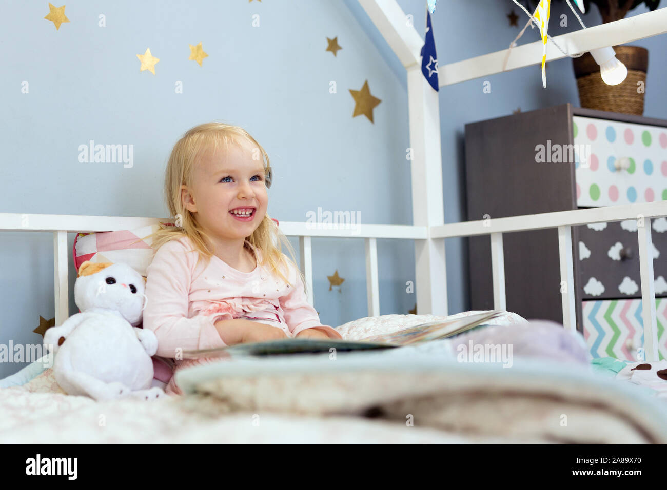 Happy little girl reading a book while sitting in bed Stock Photo - Alamy
